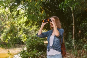 young female hiker looking through binoculars forest